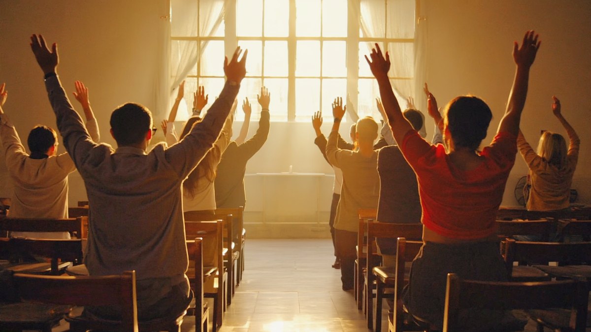 Una congregación con las manos levantadas en adoración, iluminada por la luz de una ventana